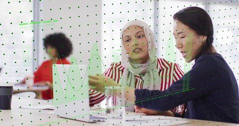 Businesswomen collaborating over laptop with green data overlay and analytics