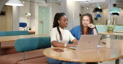 African American coworkers collaborating at modern coworking table with laptop and greenery