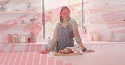 Smiling woman slicing artisan bread in modern kitchen with business chart overlay