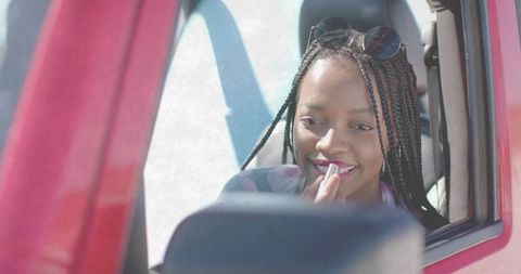 Young woman applying lipstick in car side mirror with sunglasses