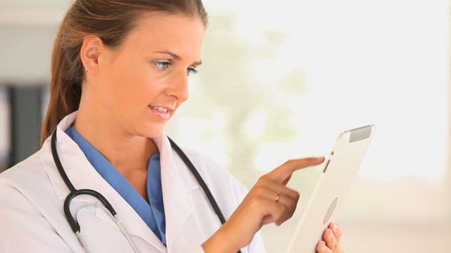 Female doctor in hospital environment using digital tablet for patient records. Perfect for articles on healthcare technology, innovative medical practices, professional work settings, and communication devices in healthcare.