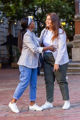African american friends greeting and laughing on urban brick plaza at twilight casual street style