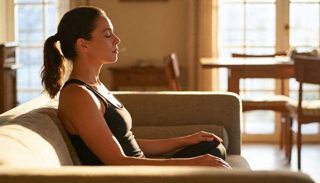 Woman meditating on sofa in sunlit living room calm mindfulness and home relaxation