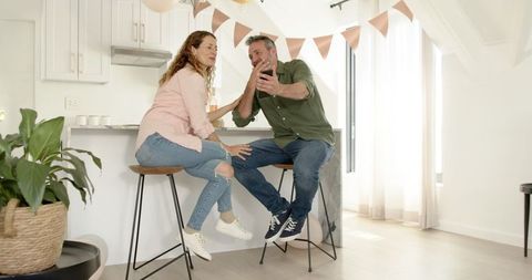 Mature Couple Sharing Laughter Over Smartphone in Bright Kitchen
