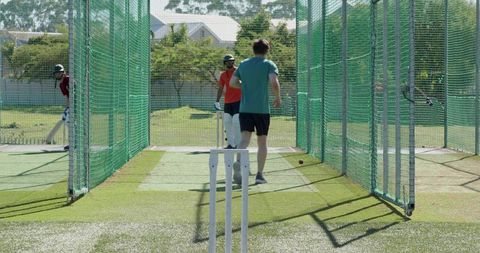 Bowler sprinting and delivering ball to batsman during cricket net practice on sunny field