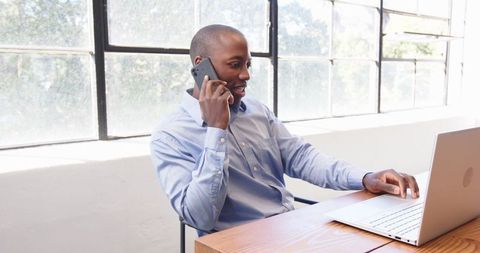 Businessman Multitasking with Smartphone and Laptop in Bright Office
