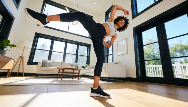 Home workout performing high side kick by athletic woman in modern sunlit living room