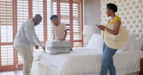 African American family packing suitcase in sunlit bedroom preparing for vacation