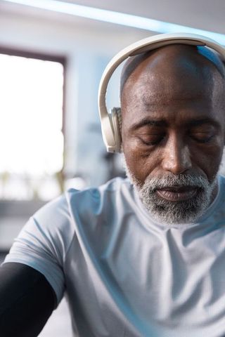 Senior african american man listening with headphones during gym cooldown, mindful recovery