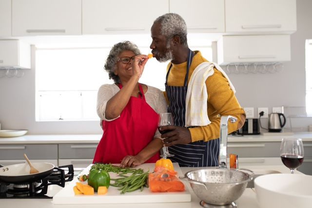 A senior African American couple at home together, social distancing and self isolation in quarantine lockdown during coronavirus covid 19 epidemic, woman feeding man in kitchen.