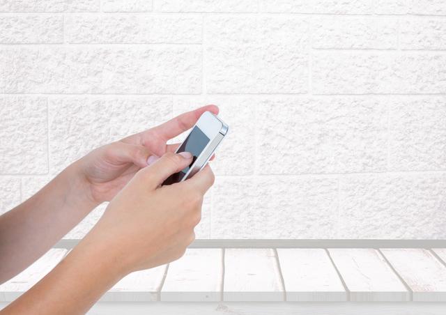 Hands holding a smartphone in front of white brick wall. Useful for promoting technology, smartphone apps, or modern communication. Can be used for marketing materials, digital advertisements, or blogs discussing mobile devices and connectivity.