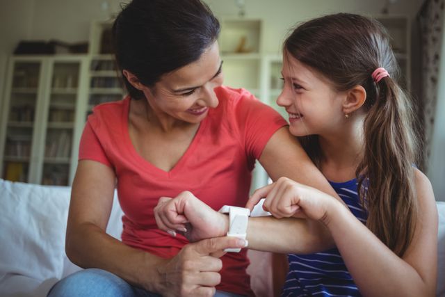 Mother and daughter smiling and interacting with a smartwatch, showcasing family bonding and use of technology. Ideal for use in advertisements for smartwatches, family-oriented products, parenting blogs, and lifestyle articles.