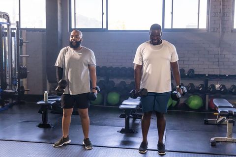African american men standing holding dumbbells smiling during partner strength training