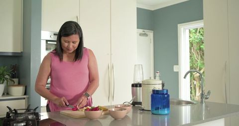 Mature woman slicing fruit on kitchen island preparing healthy smoothie