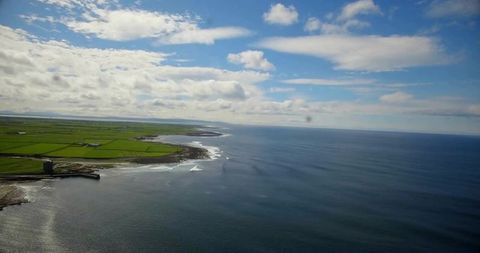 Aerial coastal panorama showing ocean meeting rocky headland with stone tower and patchwork fields