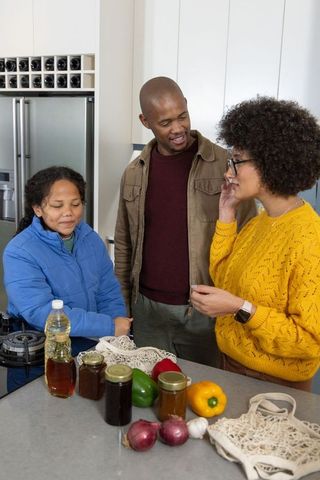 Diverse family unpacking groceries on kitchen island while woman talking on smartphone