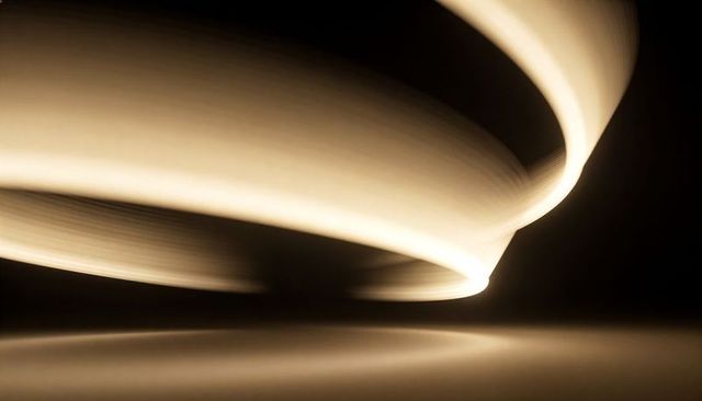 Gliding warm-white light ribbon forming smooth arc and reflection on glossy dark surface