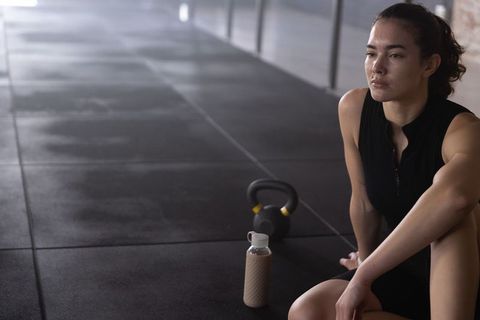 Focused fitness break woman resting after kettlebell workout in studio, hydration recovery