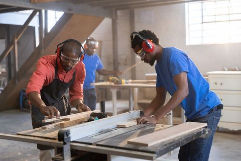 African american carpenters working table saw cutting wood planks in industrial workshop