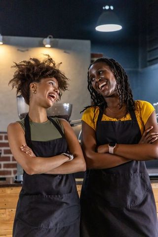 Two african american baristas laughing behind cafe counter showing teamwork and warmth