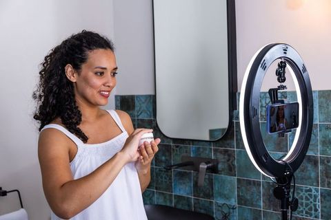 Beauty influencer recording skincare tutorial with ring light at vanity mirror