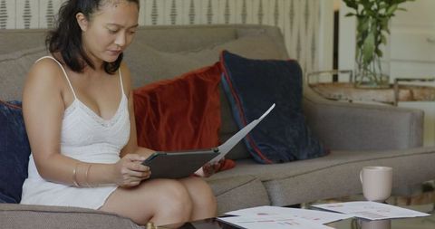 Woman Reviewing Documents with Tablet on Sofa in Modern Living Space