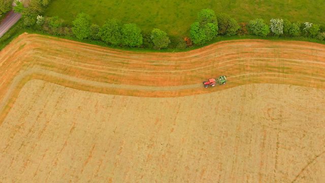 This stock video shows an aerial perspective of a tractor plowing a field surrounded by trees and green pasture, ideal for illustrating agricultural themes, farming efficiency, rural scenery, or agricultural machinery in digital and print media.