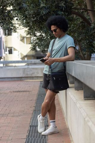 Leaning on concrete railing checking smartphone young man with afro wearing casual outfit