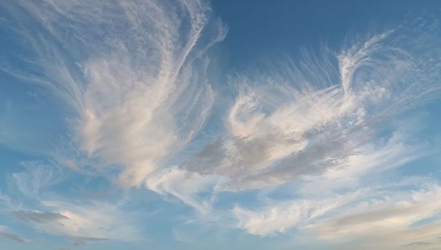 Drifting feathery cirrus clouds sweeping pastel late-afternoon sky with peach highlights