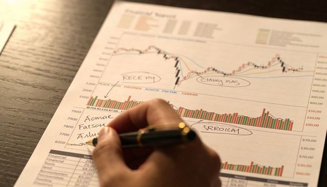 Right hand writing financial report with fountain pen on annotated stock charts and data