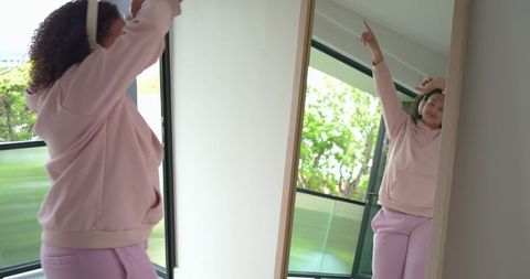 African american woman stretching in mirror wearing pink hoodie and headphones