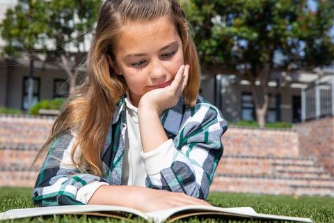 Girl reading outdoors on grass in sunny school yard