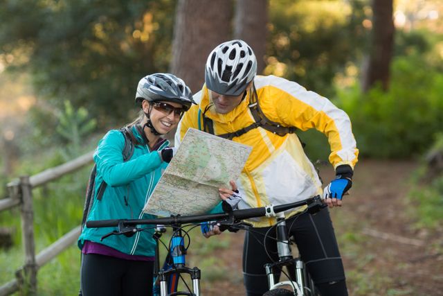 Couple wearing helmets and cycling gear, studying map while biking in forest. Ideal for promoting outdoor activities, adventure tourism, cycling events, and teamwork. Perfect for use in travel blogs, adventure magazines, and fitness campaigns.
