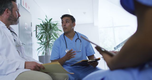 Healthcare professionals are discussing medical cases in a hospital corridor. They are wearing medical uniforms and holding patient records. The scene depicts teamwork, collaboration, and the exchange of medical knowledge among the team members. This image is ideal for illustrating healthcare teamwork, hospital environments, medical collaboration, and professional healthcare settings.