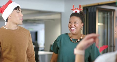 Colleagues laughing and celebrating holiday office party wearing santa hat and reindeer antlers