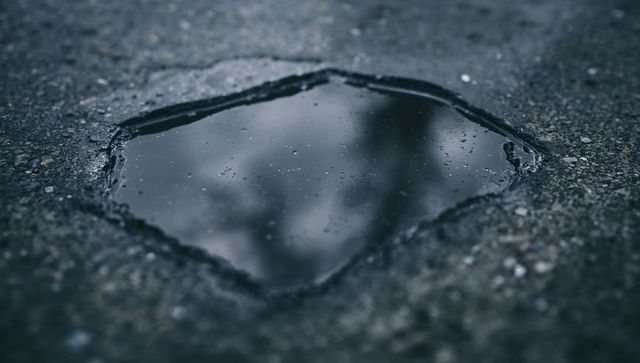 Moody puddle reflecting bare tree branches on cracked asphalt with gravel droplets