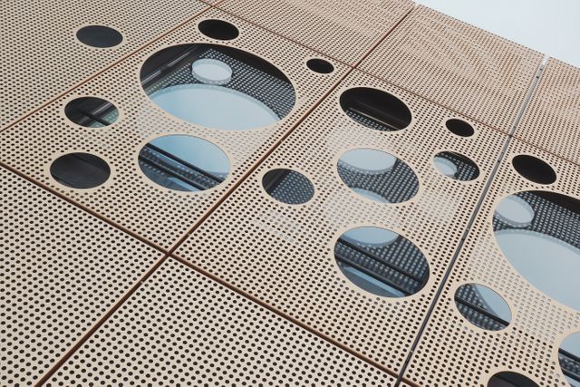 The image showcases a modern building facade featuring circular windows and perforated panels. The geometric design and innovative use of shapes create a unique aesthetic, making it ideal for urban development and contemporary architecture projects. This image can be used in articles about modern construction, architectural trends, and urban planning or as a design inspiration for architects and builders.