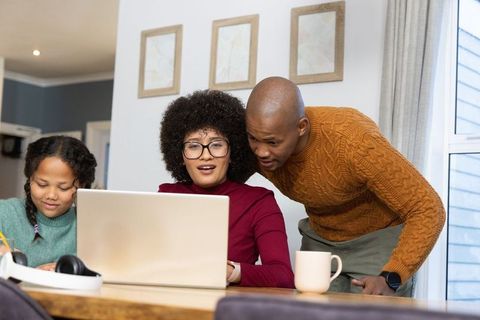 Black family working together at home kitchen table woman using laptop daughter studying
