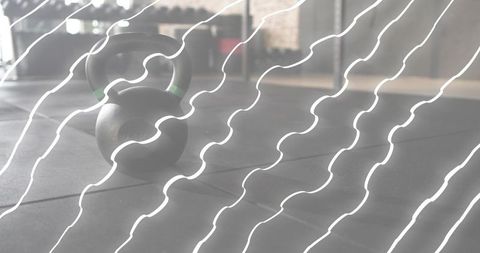 Matte-black kettlebell resting on rubber gym floor with green band and soft reflections