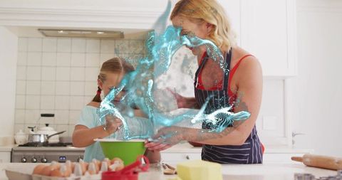 Mother teaching daughter baking with whisk and green bowl in bright white kitchen