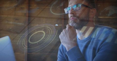 Bearded man studying laptop with holographic hud overlay in warm wooden office