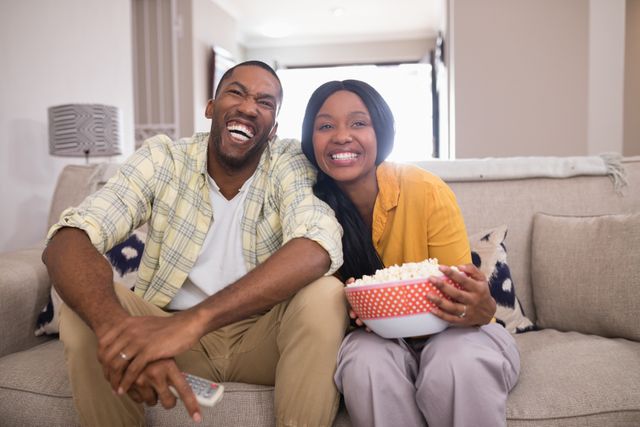 Cheerful young couple watching television while sitting on sofa at home