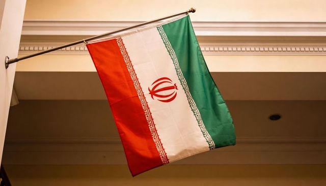 Iranian flag flying indoors on angled pole with central emblem and tricolor stripes