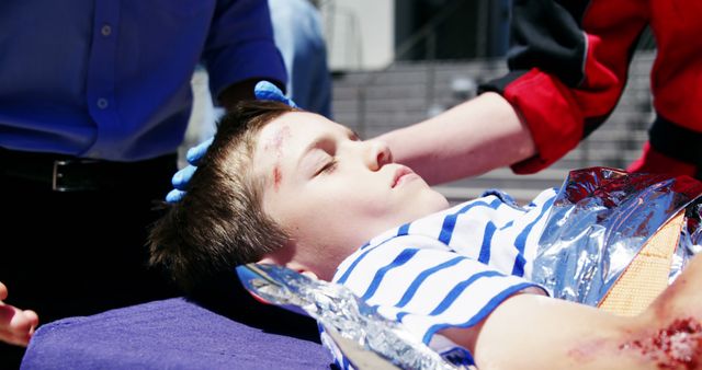 Paramedics are treating and assessing the injuries of a young boy lying on a stretcher outdoors. This is ideal for medical emergencies, healthcare, trauma response, and first aid awareness campaigns.