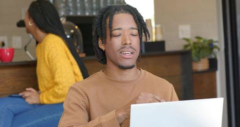 African american man working on laptop in open-plan kitchen, woman in mustard sweater