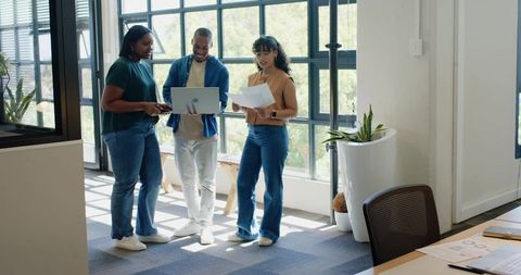 African american team collaborating in bright modern office reviewing laptop and documents