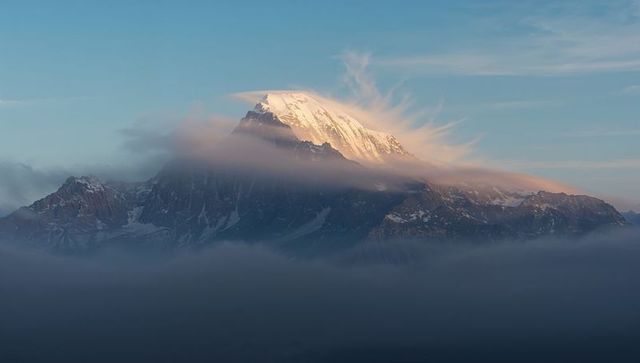 Glowing Snowcapped Summit Bathing Rugged Flanks Amid Alpine Clouds and Lenticular Plume