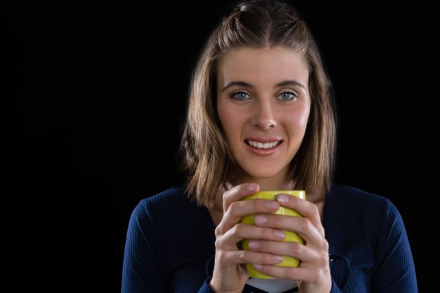 Portrait of woman holding coffee cup against black background