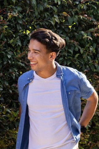 Young african american man smiling and looking left by leafy hedge in casual shirt