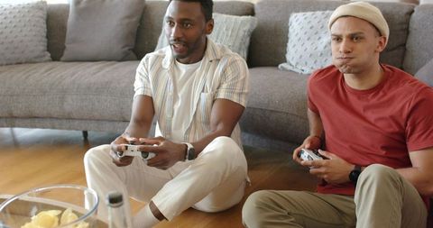 Diverse friends playing video games on living room floor with controllers and snacks